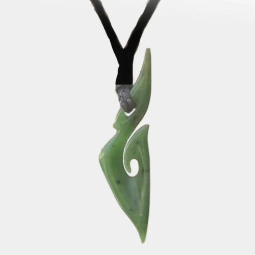 Close-up of a beautiful greenstone necklace, featuring a finely carved pendant made from pounamu, surrounded by fern leaves in a minimalist design.