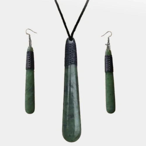 Greenstone drop pendant and matching earrings set framed by fern fronds, representing traditional Māori symbols and cultural storytelling